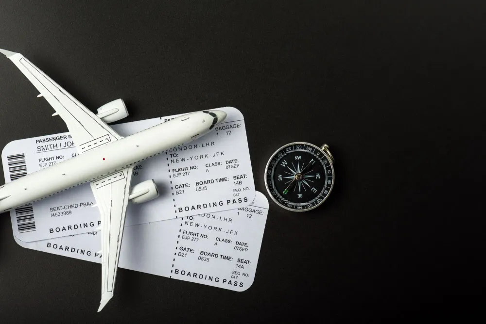 Overhead view of two boarding passes, a model plane, and a compass on a black background
